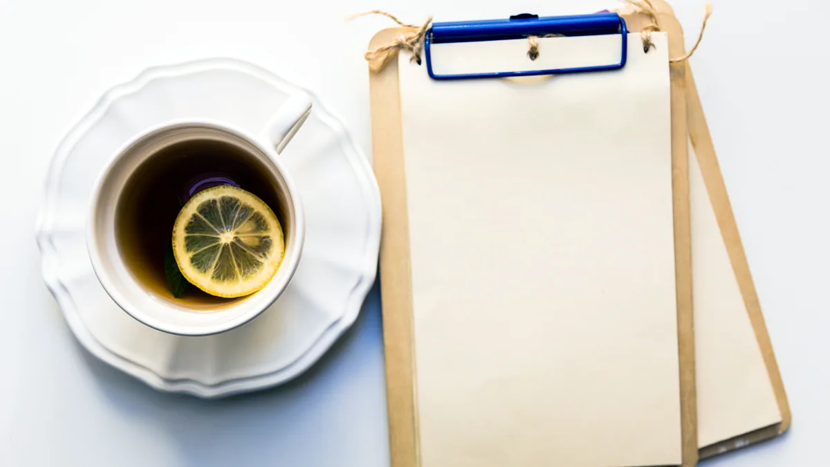 A clipboard and a warm cup of tea on a desk near a bright window.