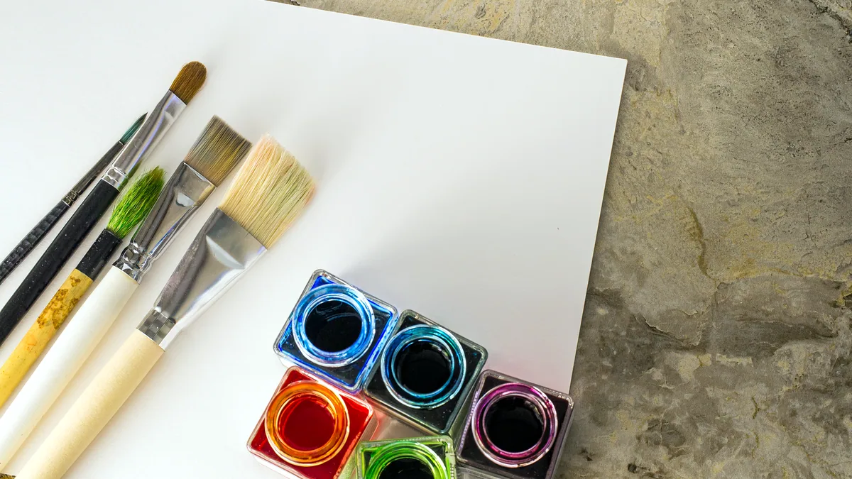 An open watercolor palette, three brushes, and a sheet of white paper.