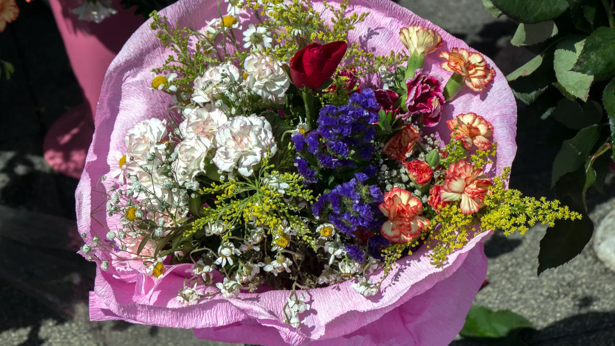 A bright wrapped bouquet of mixed flowers tied with a red ribbon.