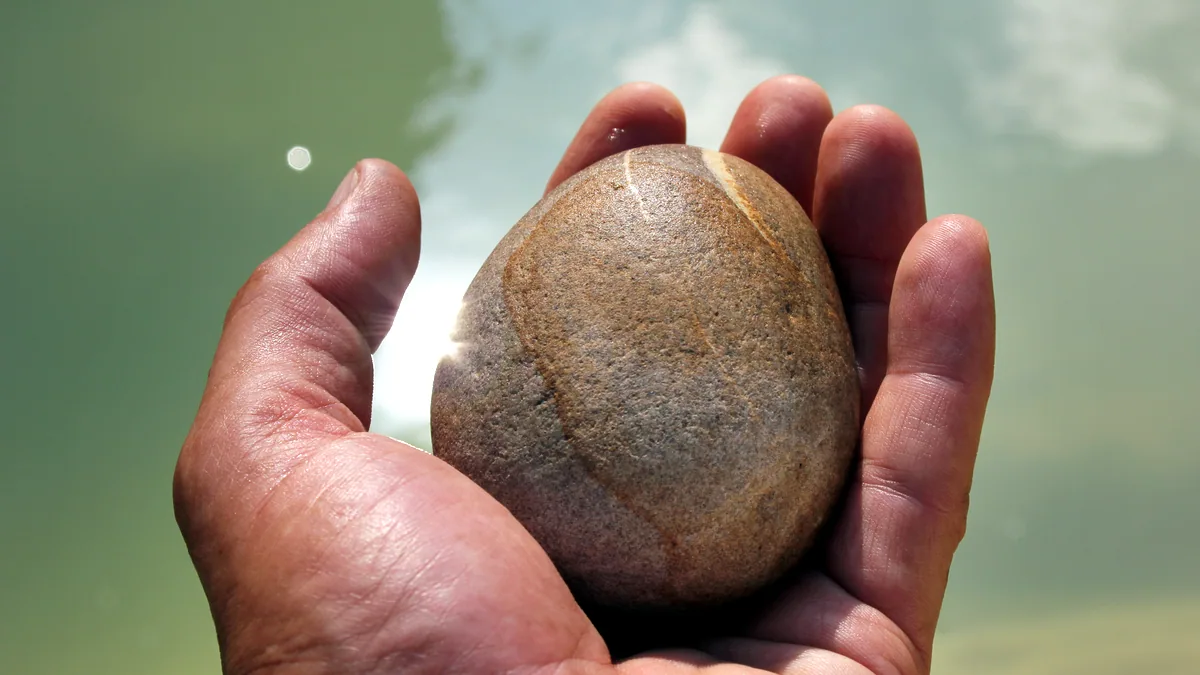 A hand holding a smooth grey river stone against soft light.