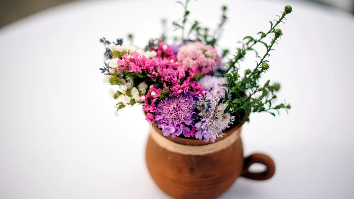 A small ceramic pot holding a posy of soft wildflowers on a stone ledge.