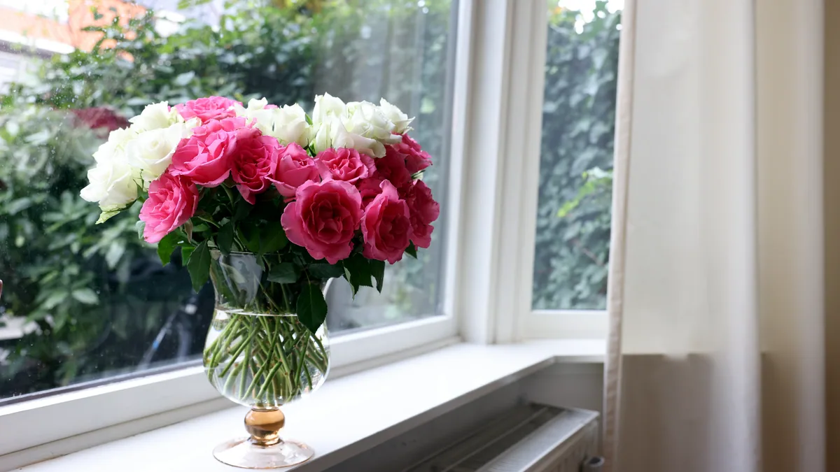 A tall vase of sunflowers and green stems on a sunny windowsill.