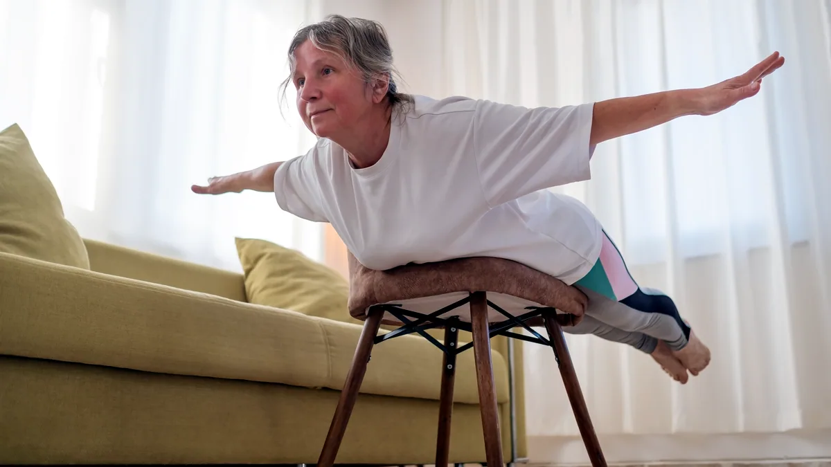An older person seated in a chair, lifting one leg straight ahead.