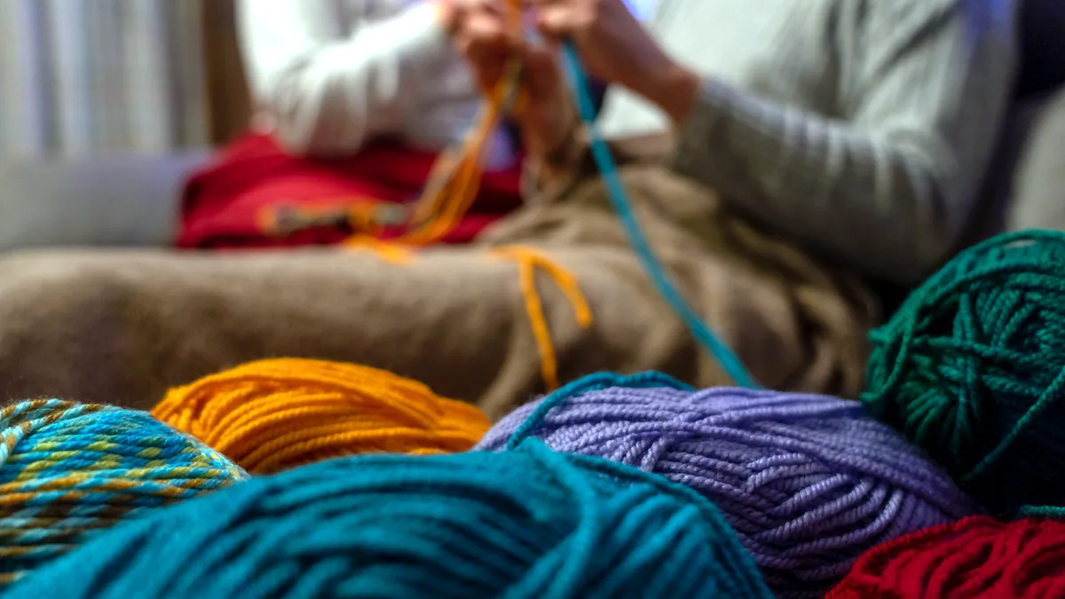 Two hands working bright multicolored yarn into a knitted scarf.
