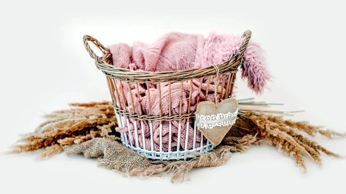 A woven basket filled with soft fabrics, wooden beads, and a smooth stone.